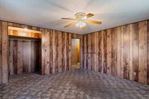 Unfurnished bedroom featuring carpet, a textured ceiling, ceiling fan, and wooden walls