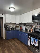 Kitchen featuring white cabinetry, blue cabinetry, appliances with stainless steel finishes, and dark wood-type flooring