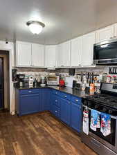 Kitchen with blue cabinetry, dark hardwood / wood-style flooring, white cabinets, and stainless steel appliances, granite countertops.