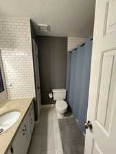 Bathroom with vanity, tile patterned floors, toilet, a textured ceiling, and walk in shower