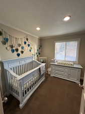 Bedroom with a crib, ornamental molding, a textured ceiling, and dark colored carpet