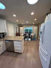 Kitchen featuring white cabinetry, white fridge with ice dispenser, light stone counters, stainless steel dishwasher, and light wood-type flooring