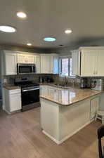 Kitchen with white cabinetry, sink, kitchen peninsula, and stainless steel appliances