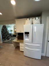 Kitchen with white cabinets, light wood-type flooring, white fridge with ice dispenser, and dark stone countertops