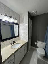 Bathroom with tile patterned floors, backsplash, a textured ceiling, toilet, and vanity