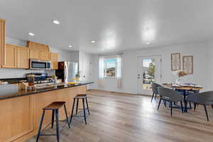 Kitchen with a kitchen breakfast bar, dark stone counters, stainless steel appliances, light brown cabinets, and light hardwood / wood-style flooring