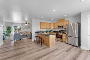 Kitchen with ceiling fan, kitchen peninsula, a breakfast bar, appliances with stainless steel finishes, and light wood-type flooring