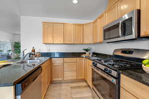 Kitchen with appliances with stainless steel finishes, light brown cabinetry, dark stone counters, sink, and light hardwood / wood-style flooring