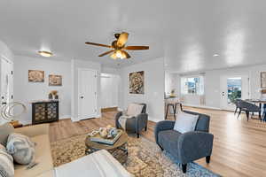 Living room with ceiling fan, a textured ceiling, and light wood-type flooring