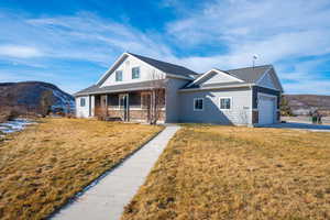 View of front of home with a mountain view, a porch, a garage, and a front lawn