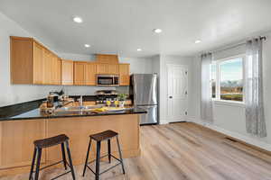 Kitchen featuring kitchen peninsula, appliances with stainless steel finishes, sink, light hardwood / wood-style flooring, and dark stone countertops