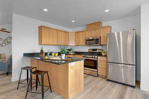 Kitchen with kitchen peninsula, appliances with stainless steel finishes, light wood-type flooring, light brown cabinetry, and ceiling fan