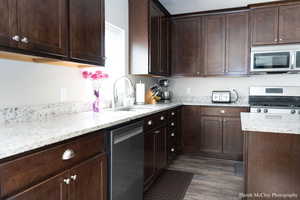 Kitchen with dark hardwood / wood-style floors, sink, dark brown cabinetry, and stainless steel appliances