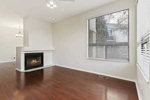 Unfurnished living room with ceiling fan with notable chandelier, hardwood / wood-style flooring, and plenty of natural light