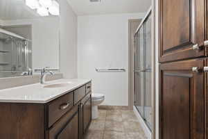 Bathroom featuring tile patterned flooring, vanity, toilet, and a shower with shower door