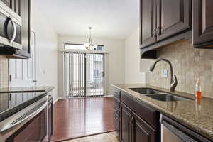 Kitchen with sink, dark hardwood / wood-style floors, decorative backsplash, dark stone countertops, and stainless steel appliances