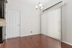 Unfurnished dining area featuring dark hardwood / wood-style flooring and a chandelier