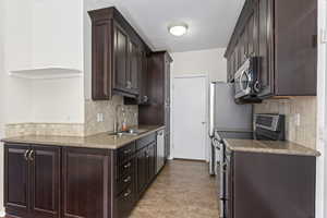 Kitchen featuring backsplash, dark brown cabinets, sink, and appliances with stainless steel finishes