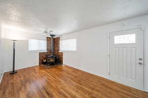 Unfurnished living room featuring a wood stove, ceiling fan, a healthy amount of sunlight, and wood-type flooring