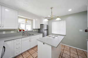 Kitchen featuring sink, decorative light fixtures, a center island, white cabinetry, and stainless steel refrigerator