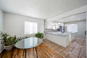 Kitchen with pendant lighting, light wood-type flooring, kitchen peninsula, and stainless steel refrigerator