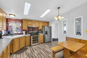 Kitchen with sink, decorative light fixtures, light hardwood / wood-style floors, stainless steel appliances, and a chandelier