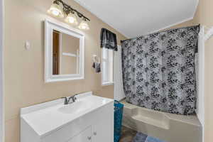 Bathroom with shower / bath combination with curtain, a textured ceiling, vanity, and vaulted ceiling