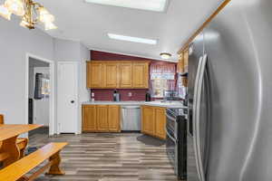 Kitchen featuring stainless steel appliances, vaulted ceiling, wood-type flooring, and a notable chandelier