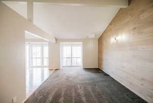 Empty room with carpet floors, wood walls, beamed ceiling, and high vaulted ceiling