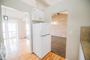 Kitchen featuring light carpet, white appliances, white cabinetry, hanging light fixtures, and wood walls