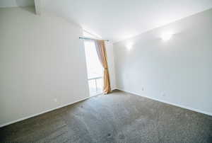 Carpeted empty room with vaulted ceiling with beams