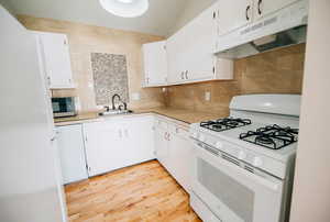 Kitchen with decorative backsplash, white appliances, sink, white cabinets, and light hardwood / wood-style floors