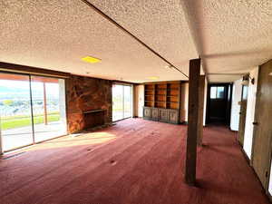 Unfurnished living room featuring a fireplace, dark carpet, and a textured ceiling