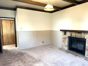 Unfurnished living room featuring beam ceiling, light colored carpet, and a brick fireplace