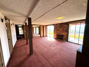 Unfurnished living room featuring carpet flooring, a stone fireplace, and a textured ceiling