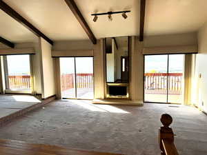 Unfurnished living room with lofted ceiling with beams, a wealth of natural light, and wood-type flooring