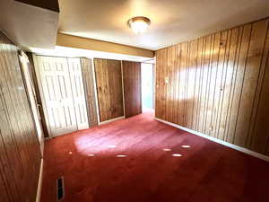 Unfurnished bedroom featuring carpet flooring, wood walls, and a textured ceiling