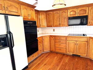 Kitchen with light wood-type flooring, tasteful backsplash, and black appliances