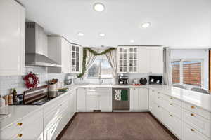 Kitchen featuring sink, dishwasher, wall chimney range hood, black electric stovetop, and white cabinets