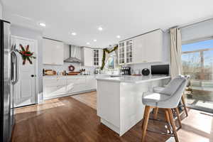 Kitchen featuring white cabinets, stainless steel refrigerator, a wealth of natural light, and wall chimney range hood