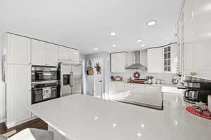 Kitchen with white cabinetry, light stone countertops, wall chimney range hood, tasteful backsplash, and stainless steel fridge with ice dispenser