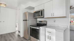 Kitchen featuring stainless steel appliances, white cabinetry, ceiling fan, and light hardwood / wood-style flooring