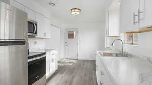 Kitchen with white cabinets, stainless steel appliances, light hardwood / wood-style floors, and sink