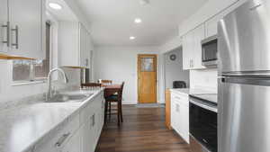 Kitchen featuring appliances with stainless steel finishes, light stone counters, dark wood-type flooring, sink, and white cabinetry