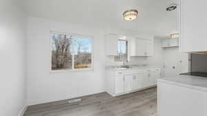 Kitchen with white cabinetry, sink, light hardwood / wood-style floors, and light stone counters