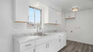 Kitchen with white cabinets, hardwood / wood-style floors, light stone countertops, and sink