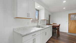 Kitchen with light stone countertops, white cabinetry, sink, and dark wood-type flooring