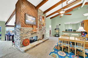 Carpeted dining room with beam ceiling, ceiling fan, a fireplace, and high vaulted ceiling