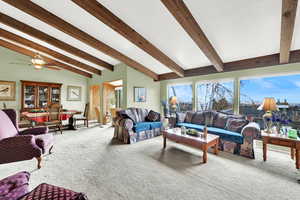 Living room with carpet flooring, vaulted ceiling with beams, and ceiling fan