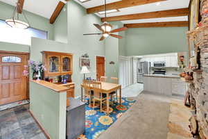 Kitchen featuring high vaulted ceiling, white cabinets, ceiling fan, beam ceiling, and stainless steel appliances